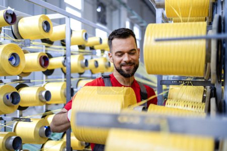 Rollos de carrete de hilo de cambio de trabajador en la máquina de tejer industrial dentro de la fábrica textil.