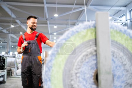 Photo for Experienced worker standing by machine and checking carpet production inside textile factory. - Royalty Free Image
