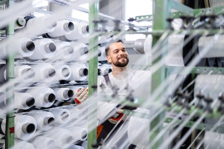 Trabajador experimentado de la fábrica textil que cambia el carrete del hilo en la máquina de tejer industrial.