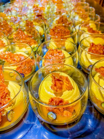 Téléchargez les photos : Exotic mousse, served with mango sauce, garnished with caramelized sugar, grape halves in a glass bowl. buffet. catering - en image libre de droit