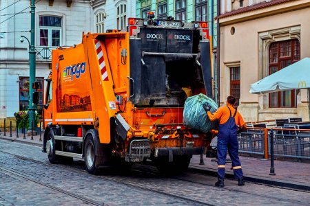 Photo for Krakow Poland August 8, 2022: garbage Collection at dawn, orange car garbage truck with worker who throws a big black garbage bag. Maintaining cleanliness and order - Royalty Free Image