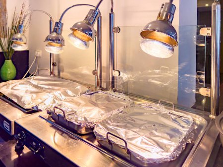 Photo for Professional Heating Equipment, Food and dish warmer, with large trays covered with foil. ideal for short-term warming up of served hot dishes, ready-made pizza, any other ready-made hot products. - Royalty Free Image