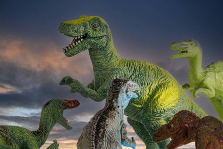 Foto de Un grupo de pequeños dinosaurios Tyrannosaurus Rex de juguete atacando a un gran tiranosaurio adulto aislado sobre un fondo de cielo al atardecer - Imagen libre de derechos