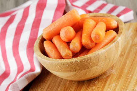 Téléchargez les photos : Gros plan d'un bol en bois rempli de délicieuses carottes bébé avec espace de copie - en image libre de droit