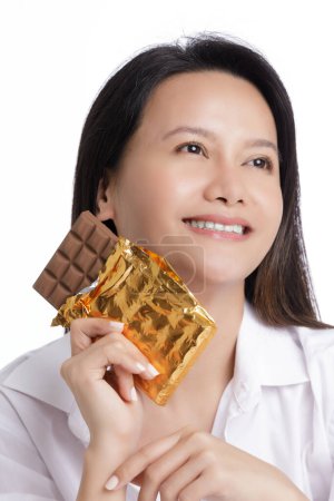 Photo for Asian American woman enjoying a Milk Chololate candy bar isolated on a white background with copy space - Royalty Free Image