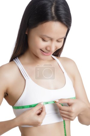 Téléchargez les photos : Belle jeune femme asiatique mesurant sa poitrine isolée sur un fond blanc avec espace de copie - en image libre de droit