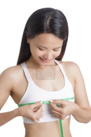 Téléchargez les photos : Belle jeune femme asiatique mesurant sa poitrine isolée sur un fond blanc avec espace de copie - en image libre de droit