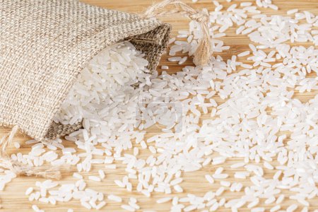 Ein Säckchen weißer Reis verschüttet sich auf einem hölzernen Schneidebrett mit Kopierraum