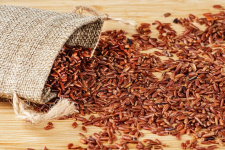 Photo for A Burlap Sack or Burlap Bag of delicious and healthy Red Rice isolated on a wooden background with copy space - Royalty Free Image