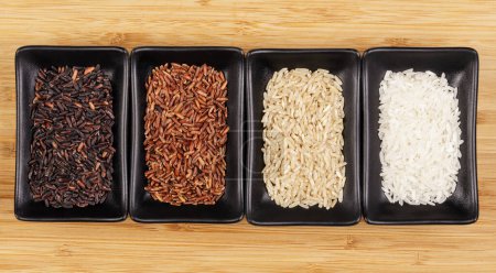 Foto de Colocación plana de cerca de cuatro tipos diferentes de arroz, negro, rojo, marrón y blanco sobre un fondo de madera con espacio de copia - Imagen libre de derechos