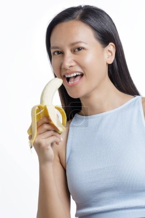 Foto de Hermosa mujer asiática comiendo un plátano sano aislado sobre un fondo blanco con espacio para copiar - Imagen libre de derechos