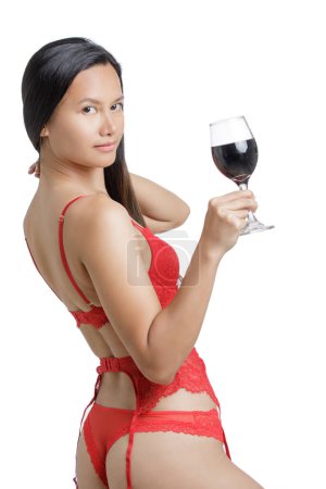 Téléchargez les photos : Jeune femme asiatique portant de la lingerie rouge et tenant un verre de vin rouge isolé sur un fond blanc avec espace de copie - en image libre de droit