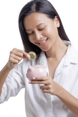 Photo for Asian American Woman saving Bitcoin into a piggy bank isolated on a white background with copy space - Royalty Free Image