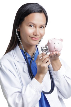 Photo for Asian American Woman Doctor examining a piggy bank, concept show the high cost of health care isolated on a white background with copy space - Royalty Free Image