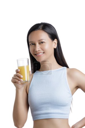 Téléchargez les photos : Asian American Woman boire un verre de jus d'orange isolé sur un fond blanc avec espace de copie - en image libre de droit