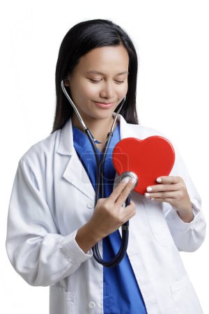 Téléchargez les photos : Asian American Woman Doctor examinant un concept Red Heart 0f Amour des soins de santé isolé sur un fond blanc avec espace de copie - en image libre de droit