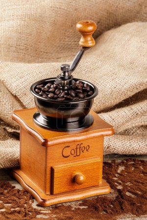 Photo for A Vintage Coffee Grinder isolated on a wooden table with a burlap back ground and copy space - Royalty Free Image