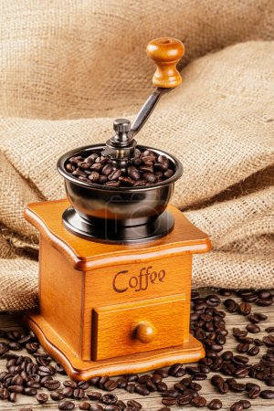 Photo for A Vintage Coffee Grinder isolated on a wooden table with a burlap back ground and copy space - Royalty Free Image