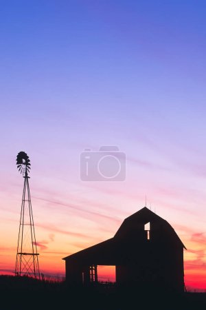 Photo for A beautiful sunset of a windmill and barn silhouetted against the evening sky in rural Indiana USA, North America - Royalty Free Image