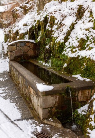 an ancient stone fountain filled with water on a snowy day