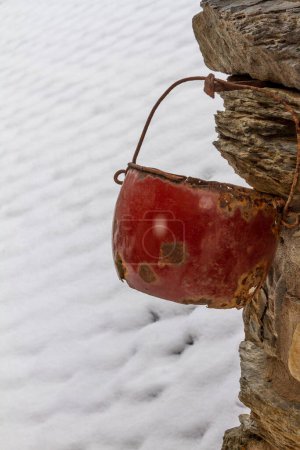 An old and worn iron pot hangs from a rural house on a snowy day