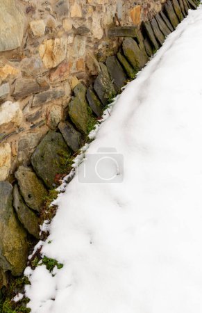 Reihe von Schieferplatten an der Wand eines steinernen Bauernhauses in einem schneebedeckten Bergdorf gestapelt