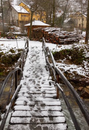 eine Holzbrücke über einen verschneiten Fluss in einem Bergdorf