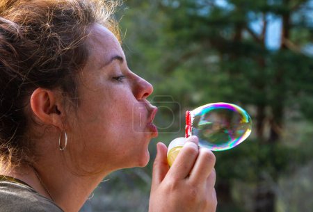 A pretty young woman plays with blowing soap bubbles on a sunny day