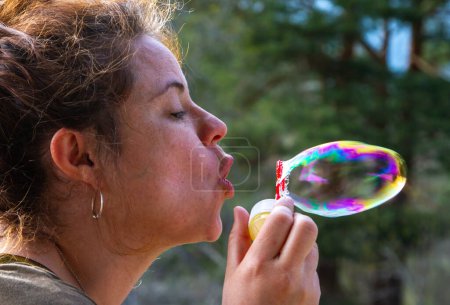 A pretty young woman plays with blowing soap bubbles on a sunny day