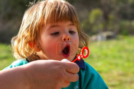 Ein hübsches zweijähriges blondes Mädchen spielt an einem sonnigen Tag mit dem Blasen blasen von Seifenblasen