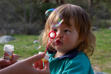 Una guapa rubia de dos años juega con burbujas de jabón en un día soleado