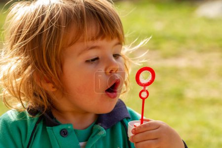 Une jolie blonde de deux ans joue avec des bulles de savon soufflantes par une journée ensoleillée