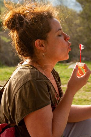 Une jolie jeune femme joue avec des bulles de savon soufflantes par une journée ensoleillée
