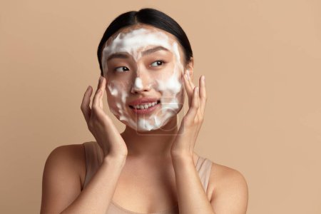 Foto de Cuidado de la piel facial. Mujer asiática linda limpieza de la piel facial con jabón de espuma. Happy Girl Cleansing Face Applying Facial Cleanser Primer plano. Alta resolución - Imagen libre de derechos