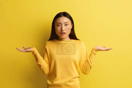 Photo for Confused Woman Shrugging Hands. Portrait of Uncertain Asian Girl Expressing Doubts and Bewilderment, Looking at Camera with Question So What, Who Cares. Indoor Studio Shot Yellow Background - Royalty Free Image