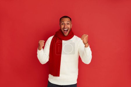 Photo for Winner Man Rejoicing Studio. Extremely Happy Multiracial Guy Raised Arm Gesturing Yes I Did It, Im Winner, Feeling Energetic and Lively. Isolated on Red Background - Royalty Free Image