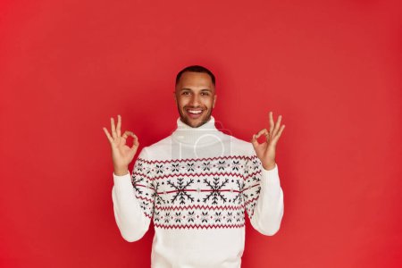 Photo for Smiling Man Showing Ok Gesture. Satisfied Multiracial Guy Making Ok Symbol with Fingers, Approving, Satisfied. Indoor Studio Shot Isolated on Red Background - Royalty Free Image