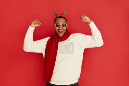 Photo for Winner Man Rejoicing Studio. Extremely Happy Multiracial Guy Raised Arm Gesturing Yes I Did It, Im Winner, Feeling Energetic and Lively. Isolated on Red Background - Royalty Free Image