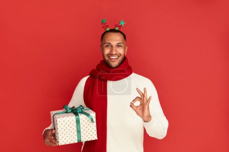 Photo for Smiling Man Showing Ok Gesture. Satisfied Multiracial Guy Making Ok Symbol with Fingers, Approving, Satisfied with Present. Indoor Studio Shot Isolated on Red Background - Royalty Free Image