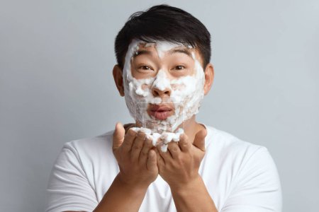 Foto de Cuidado de la piel de hombre cara. Masculino asiático limpieza facial piel con espuma jabón. Cara Limpiadora de Chico Feliz Aplicando Primeros planos Limpiador Facial. Alta resolución - Imagen libre de derechos