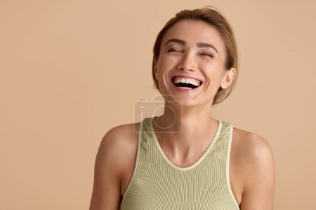 Foto de Beauty Woman Laughing Isolated Portrait. Mujer rubia modelo con piel lisa sonriendo contra fondo beige. Mujer segura disfrutando de su cuerpo perfecto después del tratamiento de cosmetología - Imagen libre de derechos