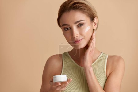 Photo for Beauty Woman Applying Face Cream. Closeup Of Female Model With Fresh Skin Holding Cream Bottle In Hand. Portrait Of Sexy Girl Applying Cosmetic Product Under Eyes. Skincare Concept. High Resolution - Royalty Free Image
