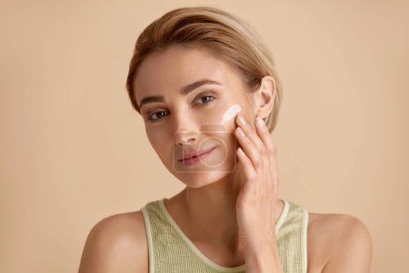 Skin Care Woman Applying Cream on Cheek. Closeup Of Beautiful Smiling Girl Putting Cream On Fresh Soft Pure Skin. Portrait Of Woman With Natural Makeup Applying Beauty Cosmetics Product 