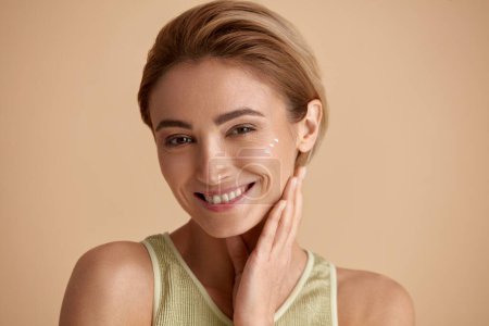 Photo for Skin Care Woman Posing with Cream on Cheek. Closeup Of Beautiful Smiling Girl with Moisturizer On Fresh Soft Pure Skin. Portrait Of Woman With Natural Makeup Recommended Beauty Cosmetics Product - Royalty Free Image
