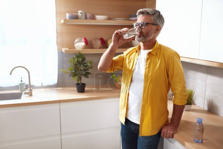 Foto de Hombre mayor bebiendo agua. Retrato de hombre maduro con vaso de agua dulce en la cocina. Concepto de salud, belleza y equilibrio hídrico - Imagen libre de derechos