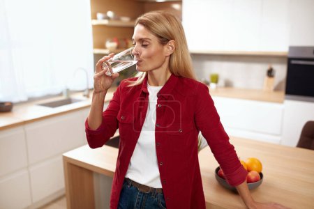 Foto de Mujer mayor bebiendo agua. Retrato de mujer sonriente feliz con vaso de agua dulce en la cocina. Salud, Belleza, Dieta y Equilibrio del Agua - Imagen libre de derechos