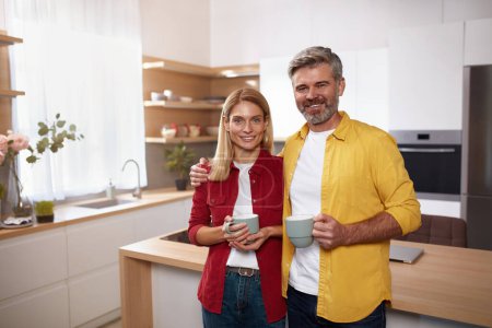 Photo for Senior Couple Holding Coffee. Happy Mature Spouses Drinking Morning Coffee And Smiling To Camera In Kitchen Interior. Man And Woman Enjoying Hot Drink - Royalty Free Image