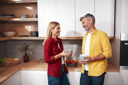 Téléchargez les photos : Couple aîné tenant du café. heureux mature conjoints boire matin café et sourire à la caméra dans cuisine intérieur. Homme et femme jouissant d'une boisson chaude - en image libre de droit