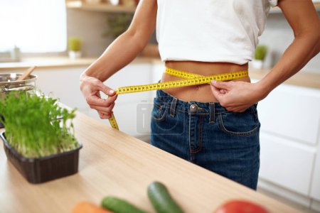 Photo for Closeup Woman Measuring Waist. Cropped View Of Diet Lady Measuring Waist With Measurement Tape At The Kitchen. Dieting concept - Royalty Free Image