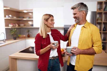 Photo for Senior Couple Holding Coffee. Happy Mature Spouses Drinking Morning Coffee And Smiling To Camera In Kitchen Interior. Man And Woman Enjoying Hot Drink - Royalty Free Image